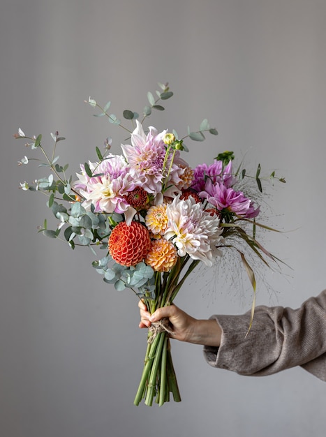 Photo a woman holds in her hand a festive flower arrangement with bright chrysanthemum flowers, a festive bouquet.