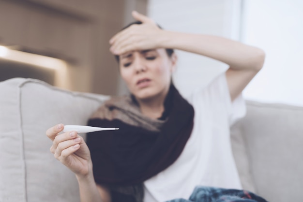 Woman holds her hand to her forehead holding thermometer.