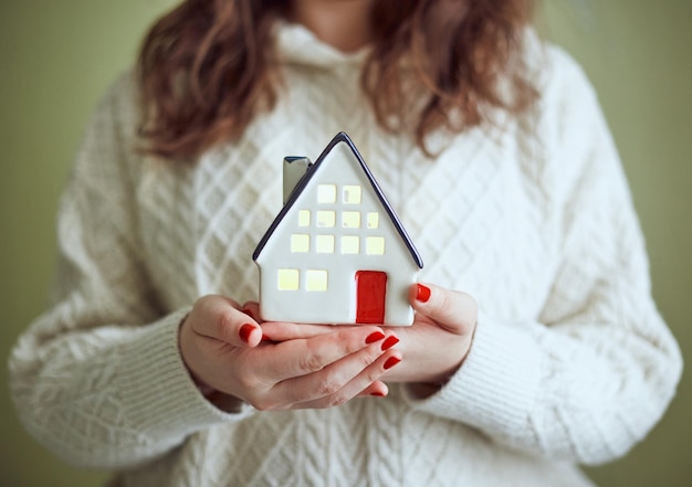 Woman holds in her hands ceramic house with light inside the concept of holiday christmas and cozine