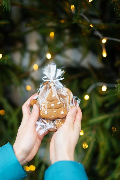 A woman holds in her hands gingerbread in the form of a Christmas tree on the background of a green Christmas tree outdoors The concept of winter holidays sweets and coziness