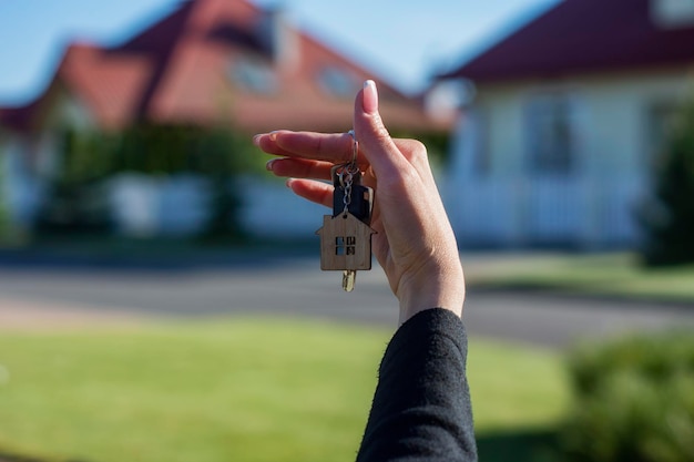 A woman holds in her hands the keys to the house against the background of residential buildings Concept for buying and renting apartments