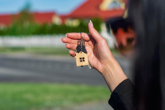 A woman holds in her hands the keys to the house against the background of residential buildings Concept for buying and renting apartments