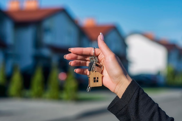 A woman holds in her hands the keys to the house against the background of residential buildings Concept for buying and renting apartments