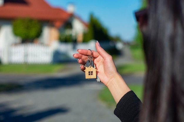 A woman holds in her hands the keys to the house against the background of residential buildings Concept for buying and renting apartments