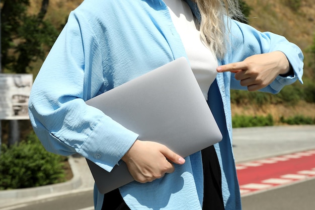 Woman holds laptop and points to him outdoor in sunny day