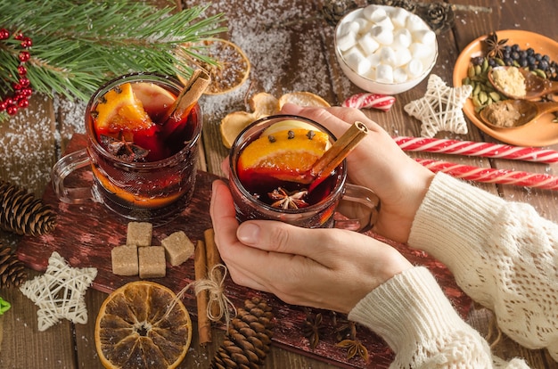 A woman holds a mug of mulled wine with an orange slice on a wooden background. Dark style