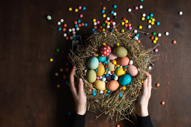 Woman holds a nest with colorful Easter eggs and chocolate candies Easter decoration