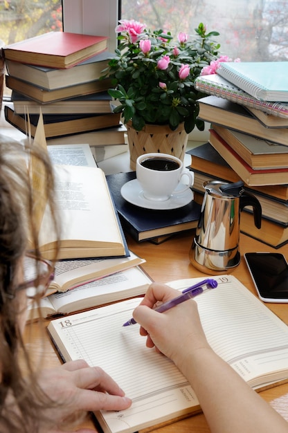 A woman holds a pen and takes notes in a notebook on a desk in her office surrounded by books