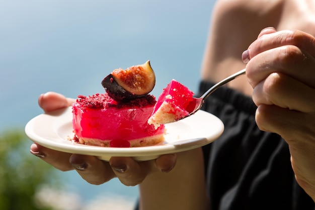 Photo a woman holds a plate with a cake poured with red jelly with figs on the background sea