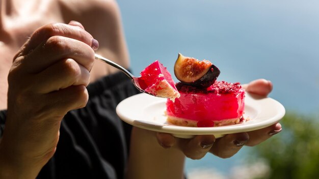 Photo a woman holds a plate with a cake poured with red jelly with figs background of the sea