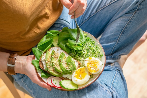 A woman holds a plate with useful healthy foods avocado cucumber spinach radish egg microgreens