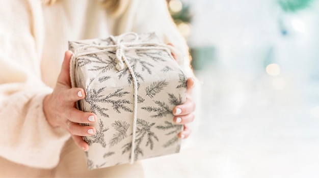 A woman holds a present box in her hands on a Christmas evening next to a Christmas tree