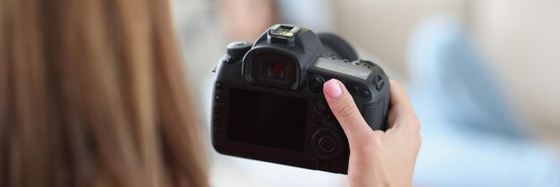 Woman holds professional black camera in hands and photographs model at home