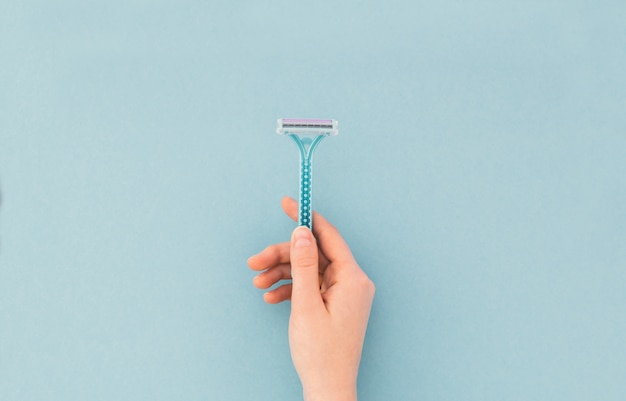 Woman holds a razor in her hand on blue. Copyspace