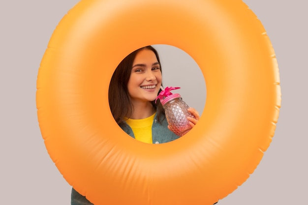 Woman holds rubber ring in hands and drinking tropic cocktail on vacation in resort looks at camera