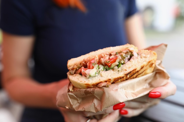 A woman holds a sandwich with a filling in a paper bag ordering lunch at fast food catering for