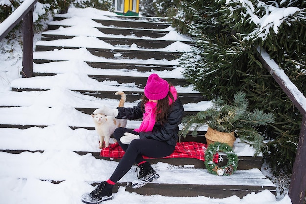 Woman holds and strokes white furry cat near Christmas tree Domestic pet enjoys affection and attention New Year's magical atmosphere of comfort love and warmth