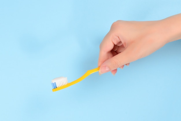 Woman holds toothbrush with toothpaste in her hand on a blue background.