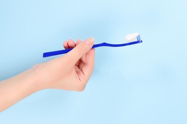 Woman holds toothbrush with toothpaste in her hand on a blue