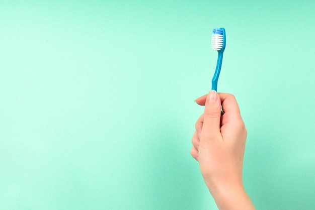 The woman holds toothbrushes in her hand on a green background.