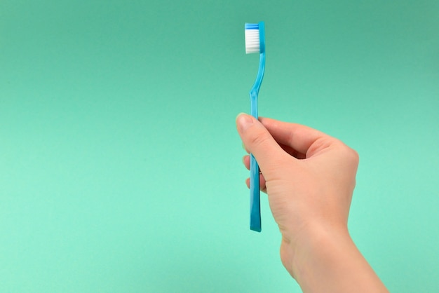 The woman holds toothbrushes in her hand on a green background.