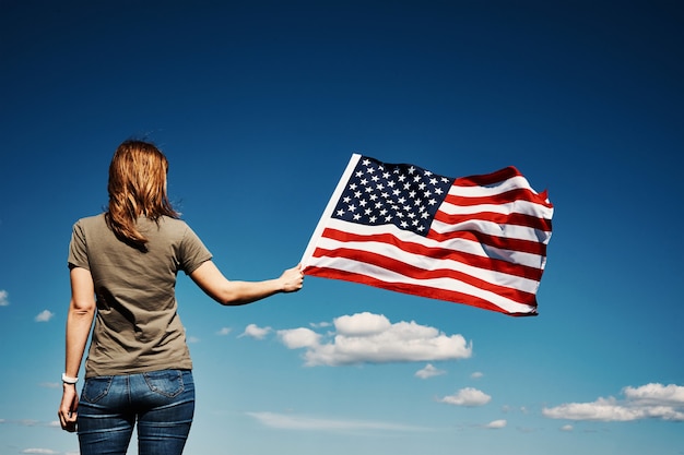 Woman holds usa national flag against blue cloudy sky