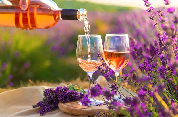 A woman holds wine in glasses. Picnic in the lavender field. Selective focus.