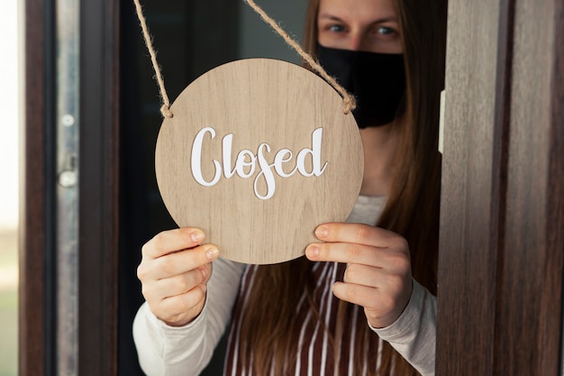 Woman holds the wooden sign with text: Closed