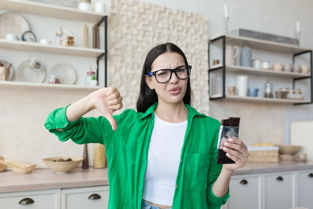 Woman at home disapproving of a bar of chocolate looking at the camera and pointing a finger down