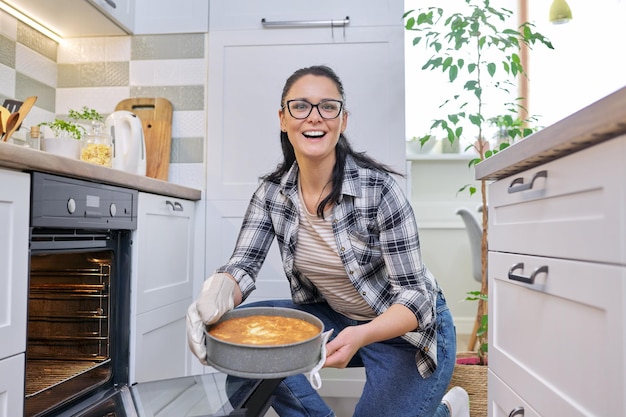 Woman at home in kitchen taking out hot apple pie from oven