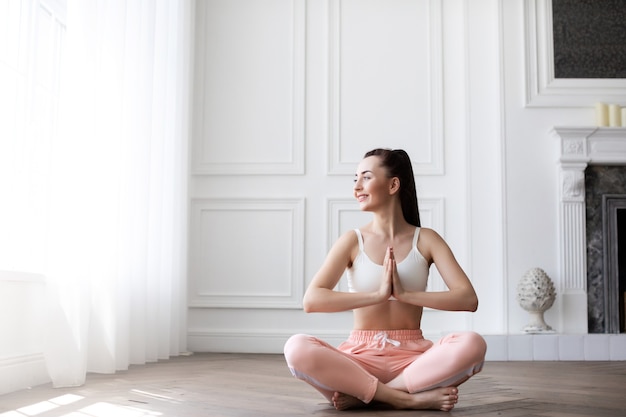 Woman at home in the lotus position. Portrait of young happy girl practicing yoga.