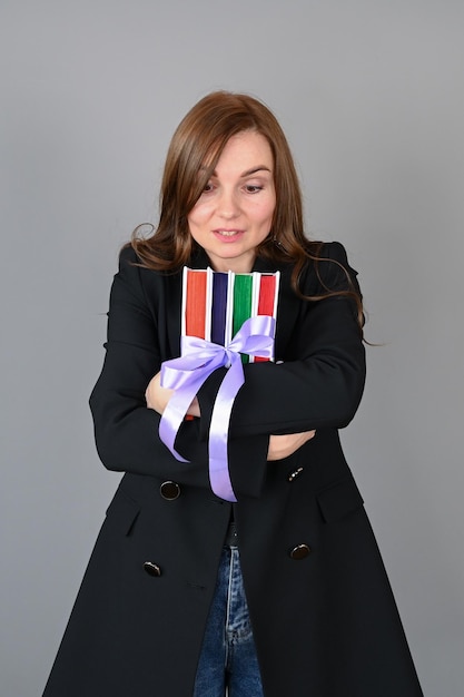 Woman hugs a stack of colorful books on gray background educational course concept