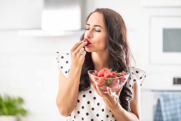 Woman indulges in a taste of a fresh strawberry holding bowl full of freshly picked harvest.