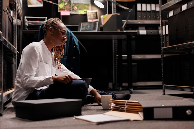 Woman investigator solving crime while sitting on floor in police office room. Private detective analyzing case file, studying information and searching evidence in agency