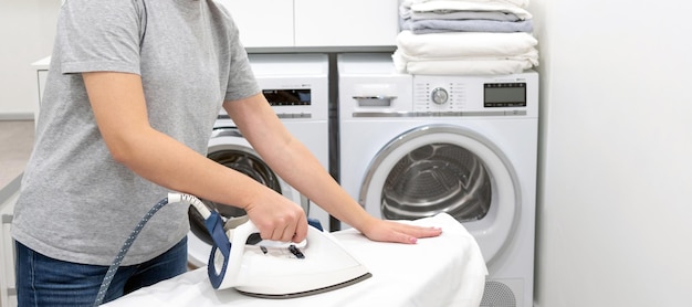 Woman ironing on board in laundry room with washing machine on background