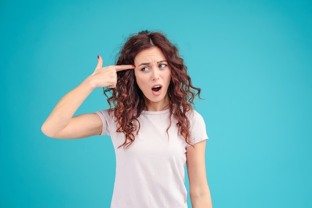 Woman is annoyed and ready to shoot herself isolated over blue background