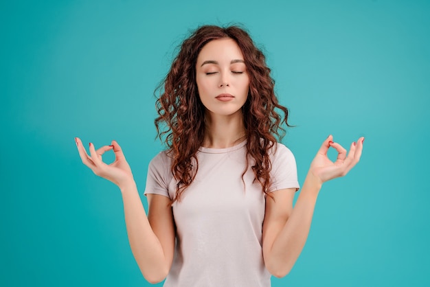 Woman is calm and relaxed with zen gestures isolated over turquoise blue background