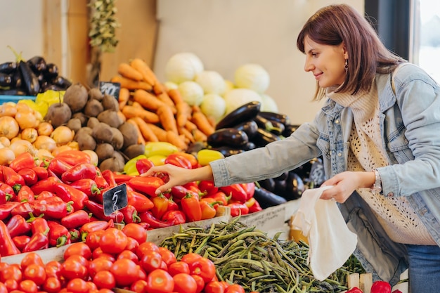 Woman is chooses fruits and vegetables at food market. Reusable eco bag for shopping. Sustainable lifestyle. Eco friendly concept.