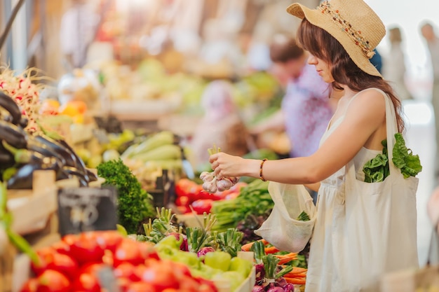 Woman is chooses  fruits and vegetables at food market. Reusable eco bag for shopping. Zero waste concept.