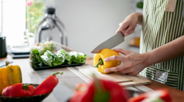 Woman is cooking in home kitchen Female hands cut bell pepper vegetables greens tomatoes on table on wooden boards Healthy food salad or vegetarian food