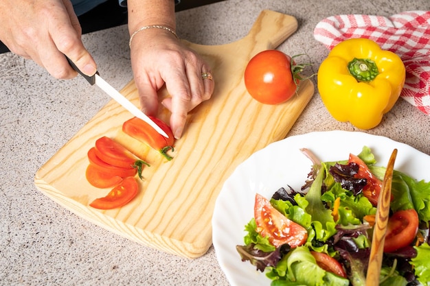 A woman is cutting tomatoes on a cutting board with a bowl of salad on the table