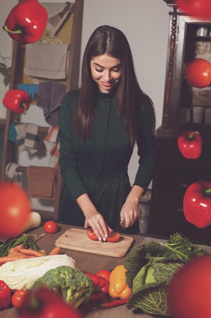 Woman is cutting tomatos at the table with different vegetables