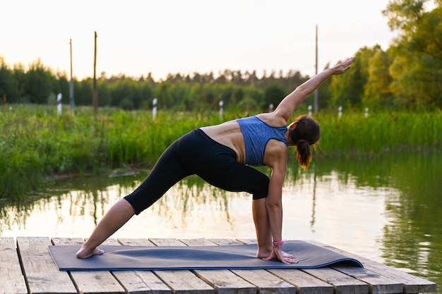 A woman is doing exercises on the lake in nature. The concept of keeping fit.