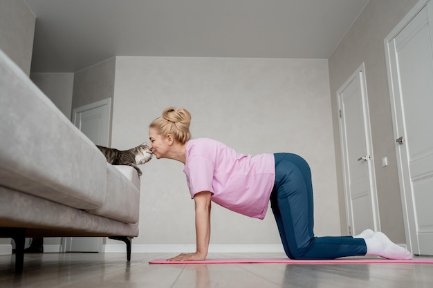 A woman is doing yoga at home bonding with her cat comforting routine workout with a feline