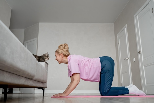 A woman is doing yoga at home bonding with her cat comforting routine workout with a feline