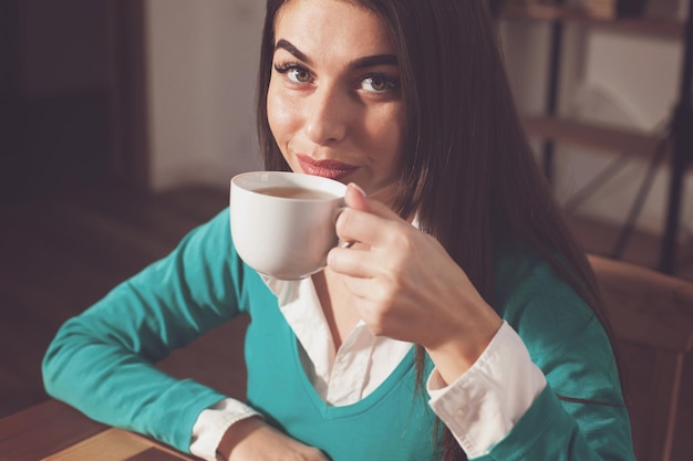 Woman is drinking a cup of coffe at the wood table