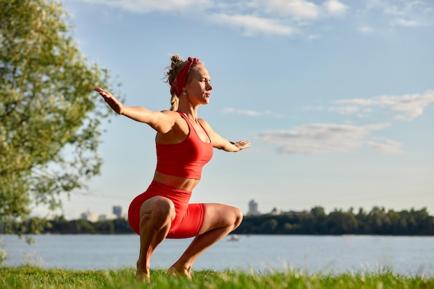 A woman is engaged in animal flow gymnastics closeup outdoors near the river on green grass in red clothes