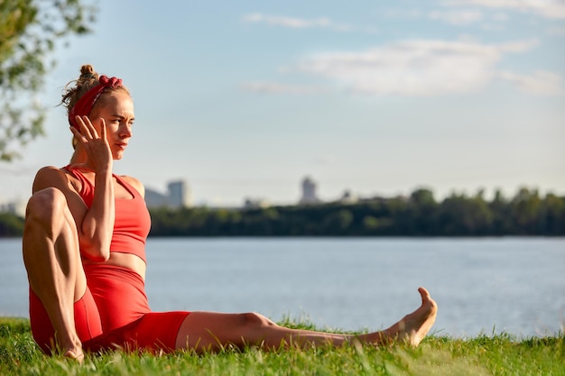 A woman is engaged in animal flow gymnastics closeup outdoors near the river on green grass in red clothes