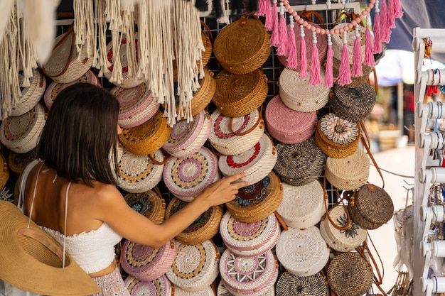 Woman is enjoying her trip to exotic country and cjoosing gift among wicker bags in small street shop