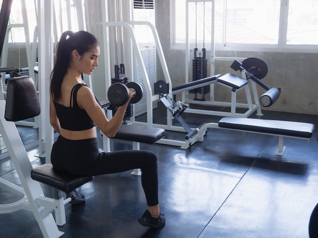 Woman is exercising with a dumbbell in gym